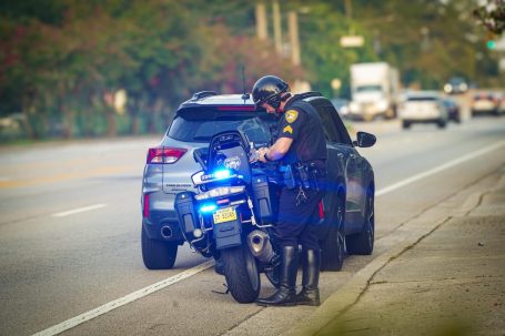 A motorcycle officer interacting with a parked car on the roadside.