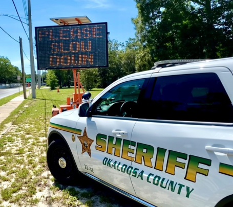 Sheriff's vehicle parked beside a sign displaying "PLEASE SLOW DOWN."